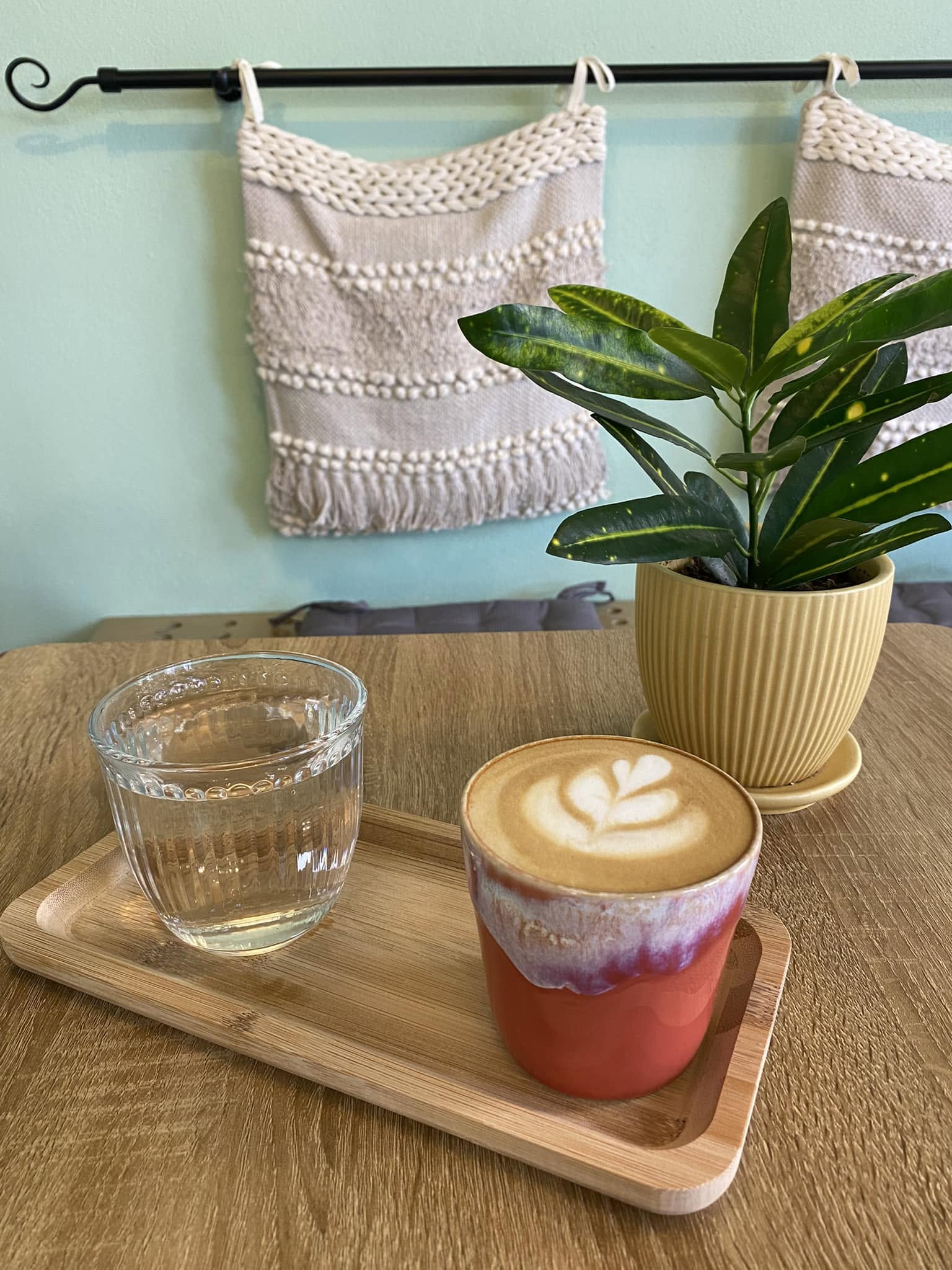 Cappuccino și apă pe o tavă din lemn, în interiorul cafenelei MWAKI cu plante și decorațiuni textile